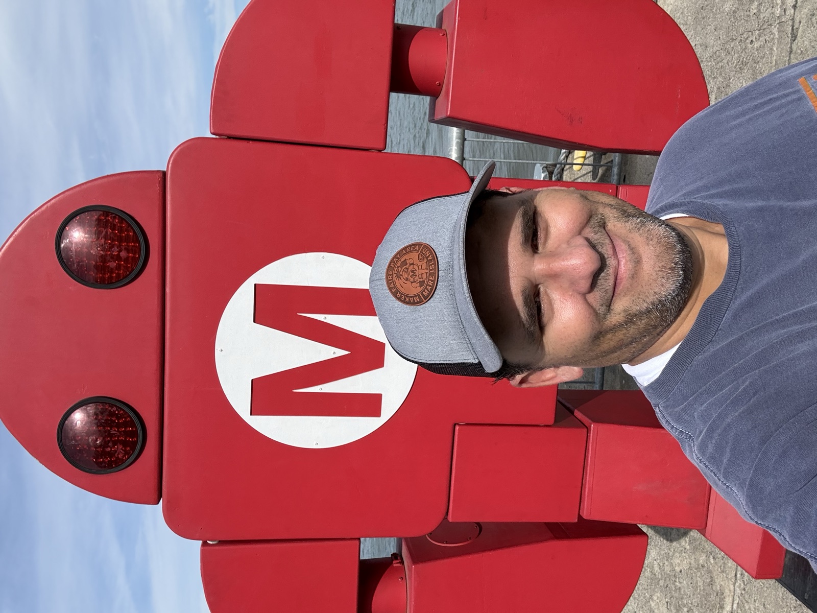 Selfie of Mario Cruz in a Maker Faire Bay Area Mare Island cap in front of the giant red Makey robot